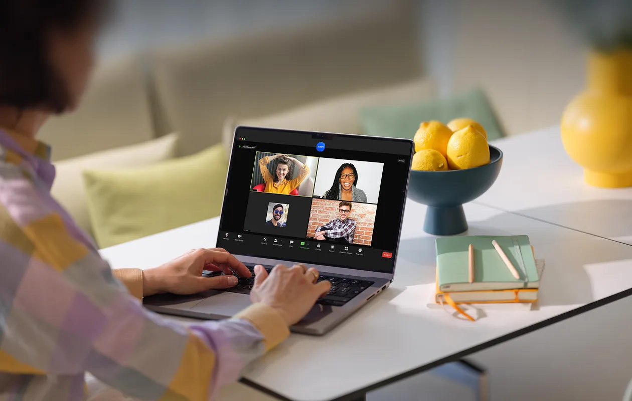 Person using a laptop to participate in a video conference call with four smiling participants on screen.