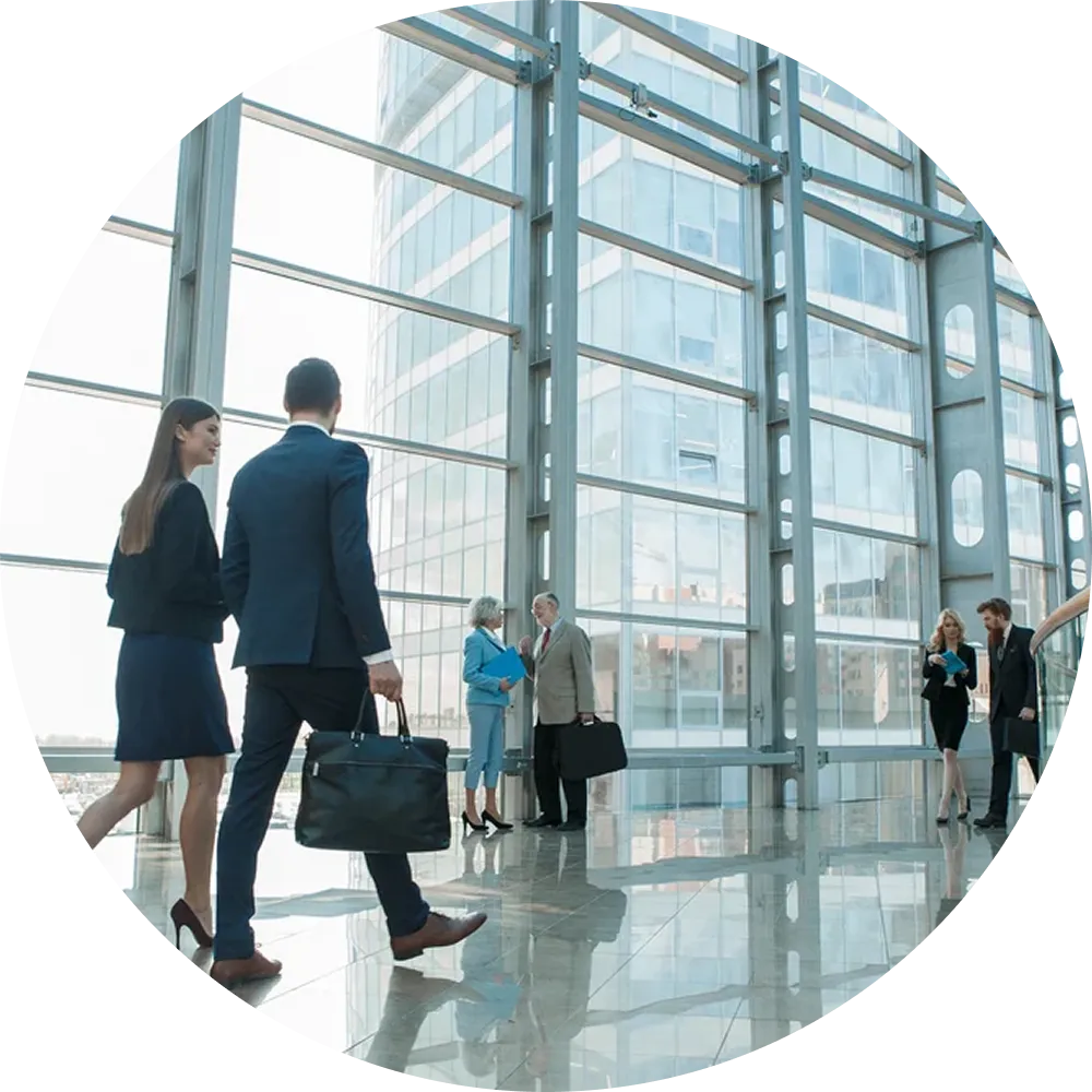 Business professionals walking and conversing in a modern office lobby with large glass windows.