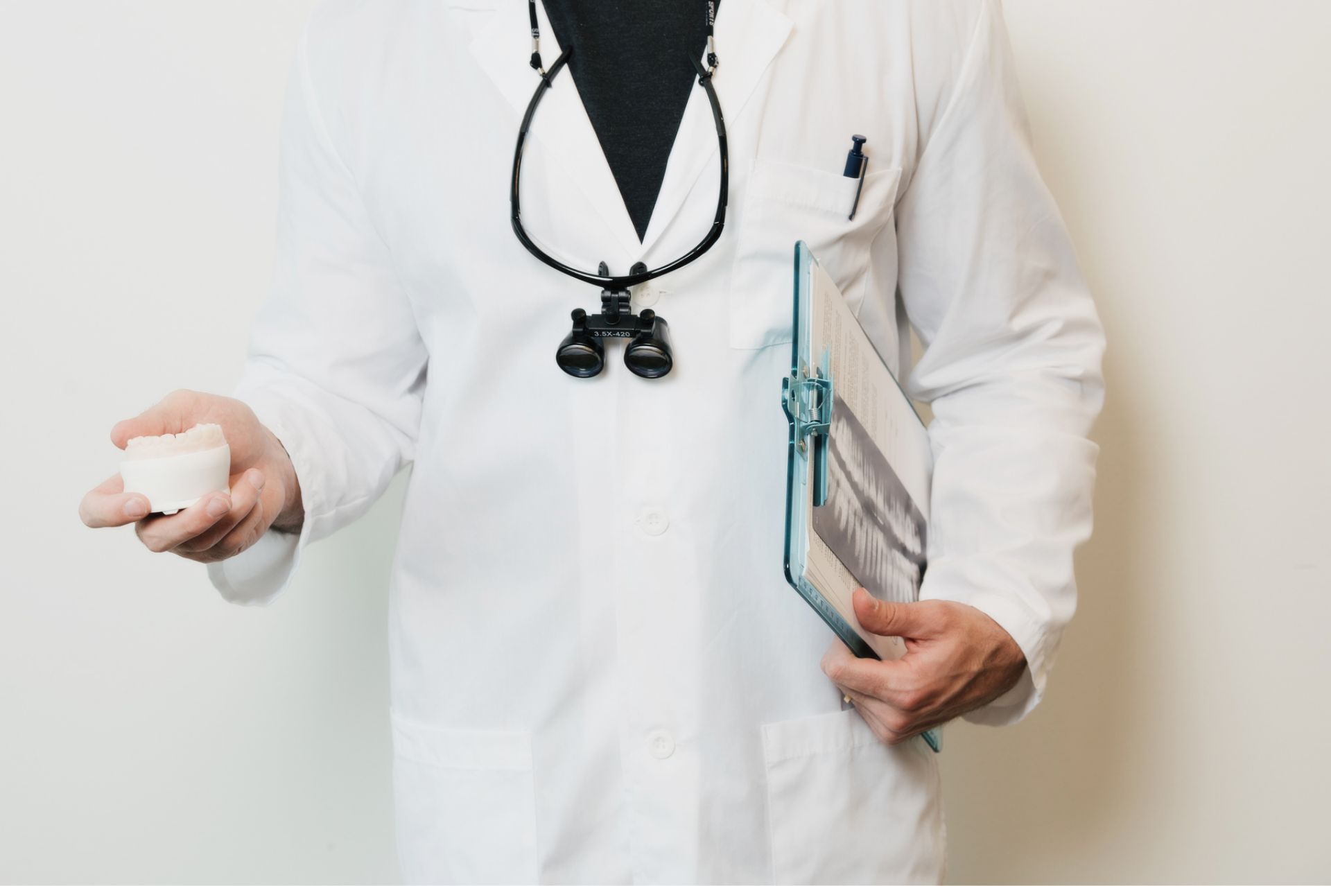 Dentist in a white coat holding a dental mold in one hand and a clipboard with dental x-rays in the other.