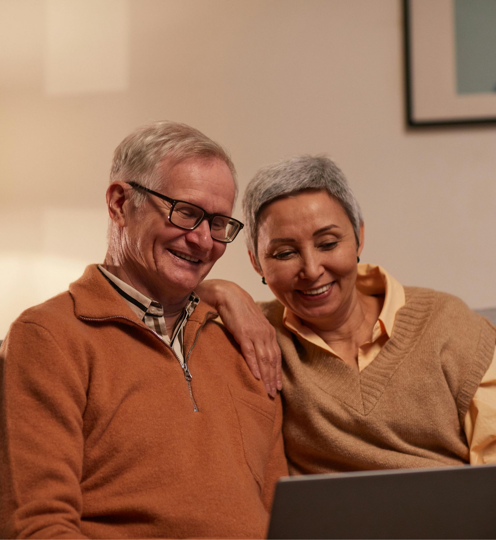Smiling older couple sitting close and looking at a laptop screen together.