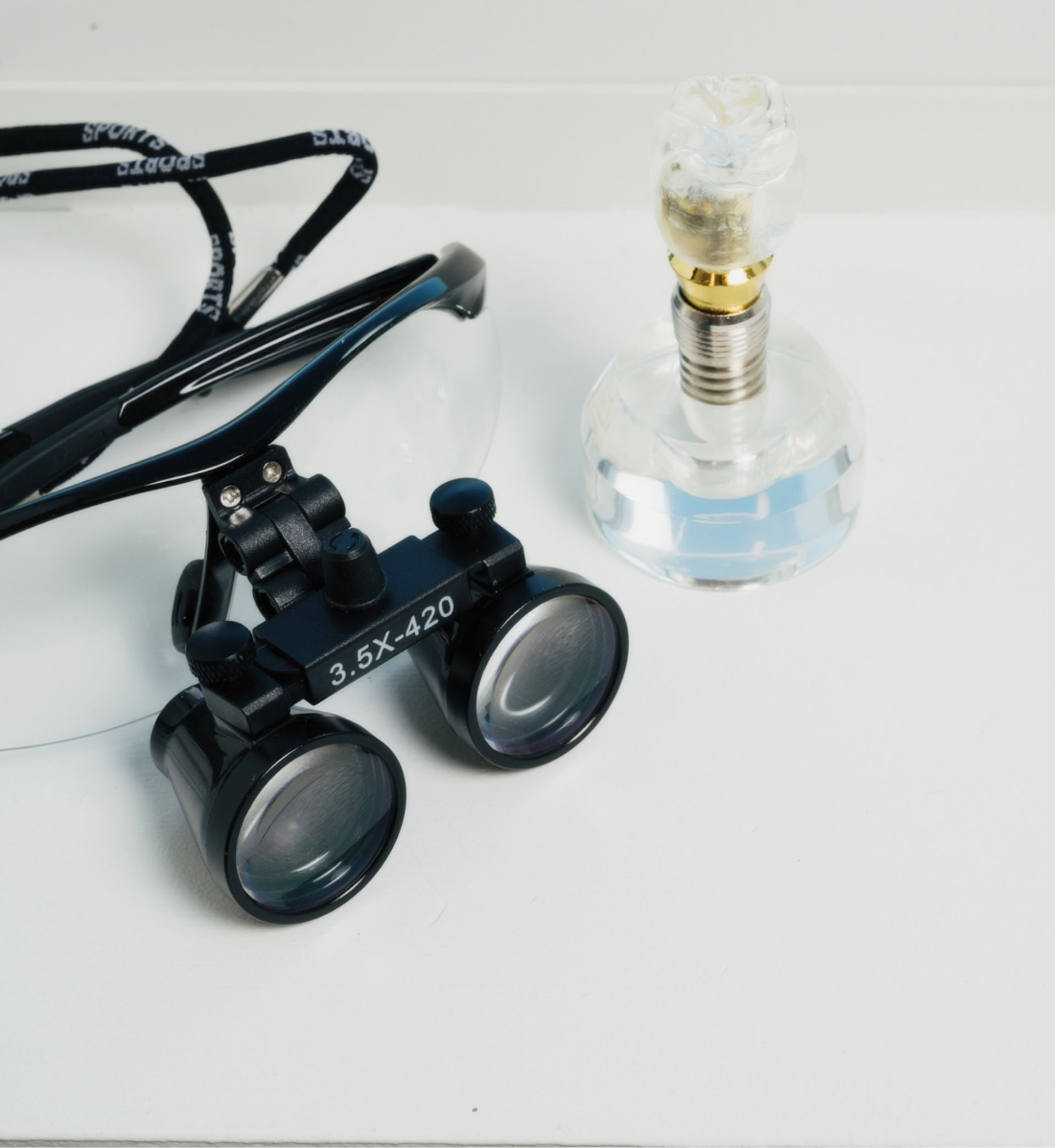 Dental magnifying glasses labeled 3.5X-420 and a clear dental model on a white surface.