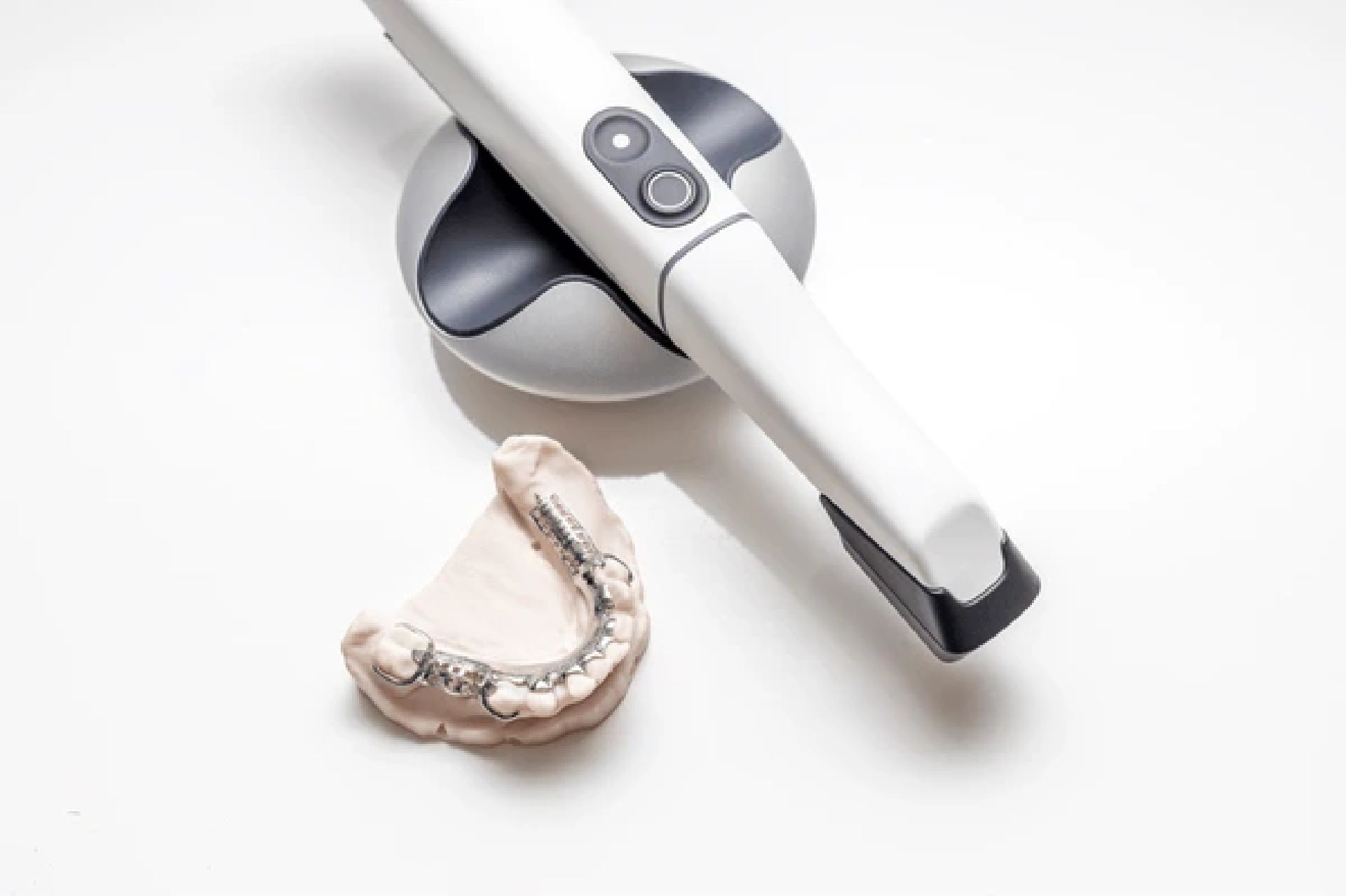 Dental model with metal braces next to a white and black intraoral scanner on a white background.