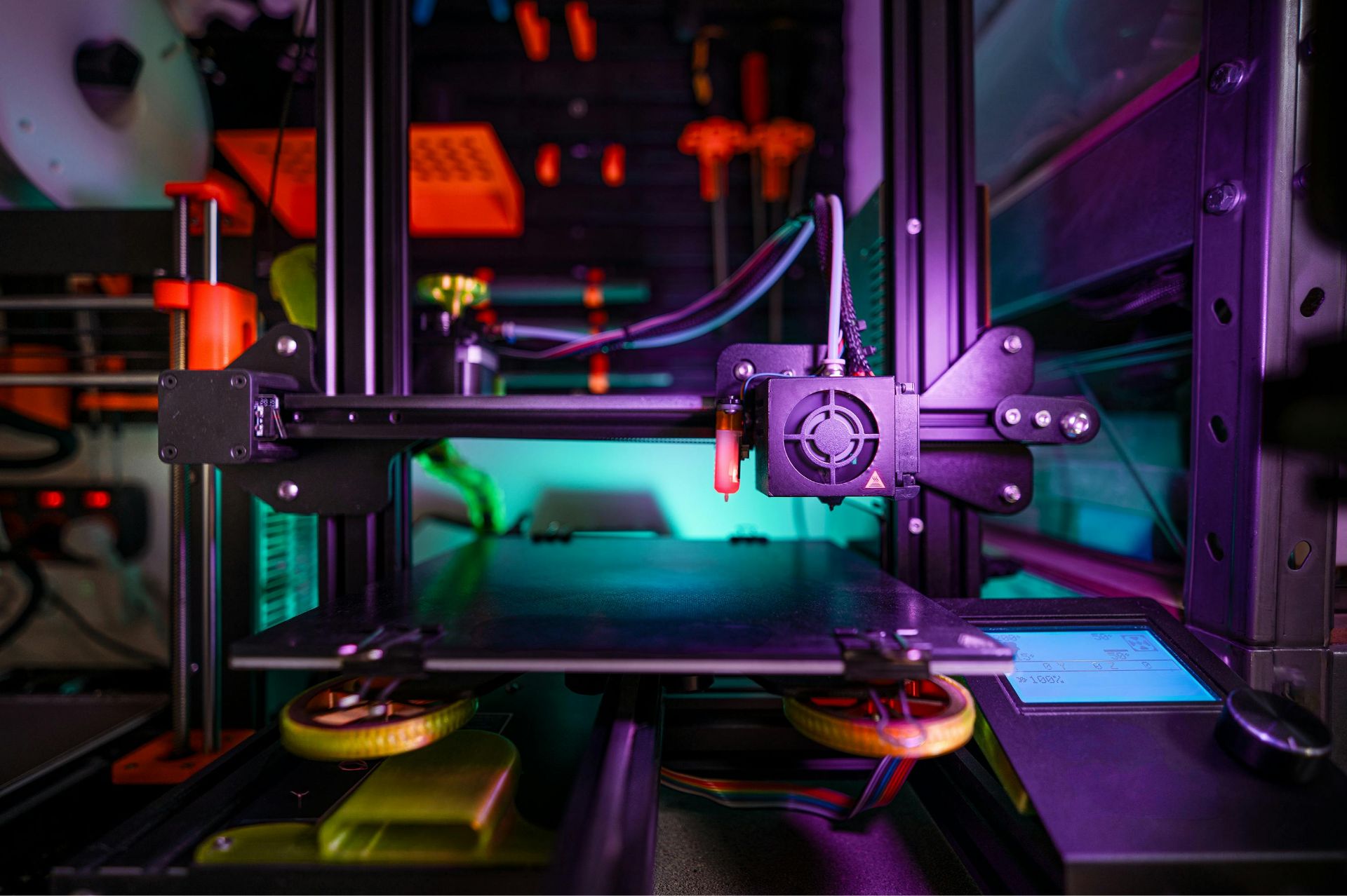 Close-up of a 3D printer's print bed, print head, and control screen under purple and teal lighting.
