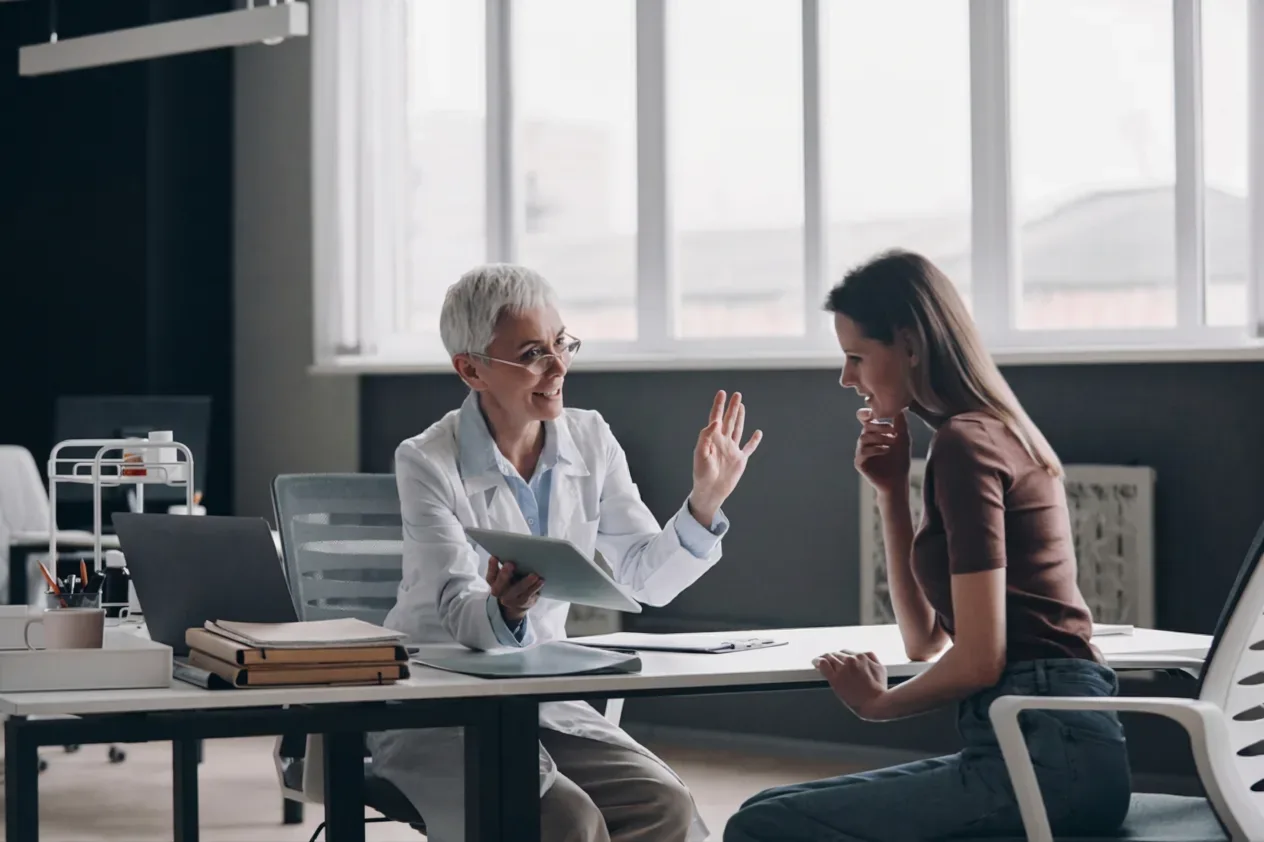 A physician with a tablet talking with a patient across a desk