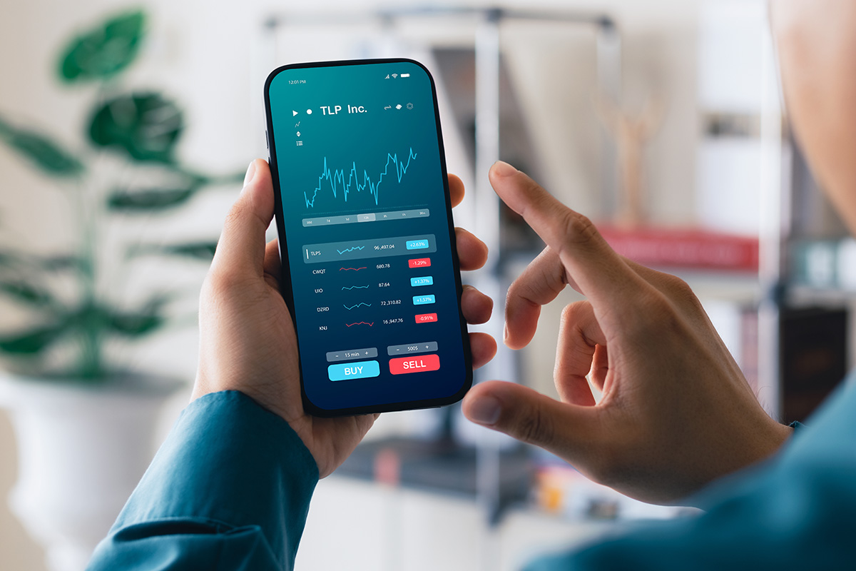Person holding smartphone displaying stock market app with charts and buy/sell buttons.