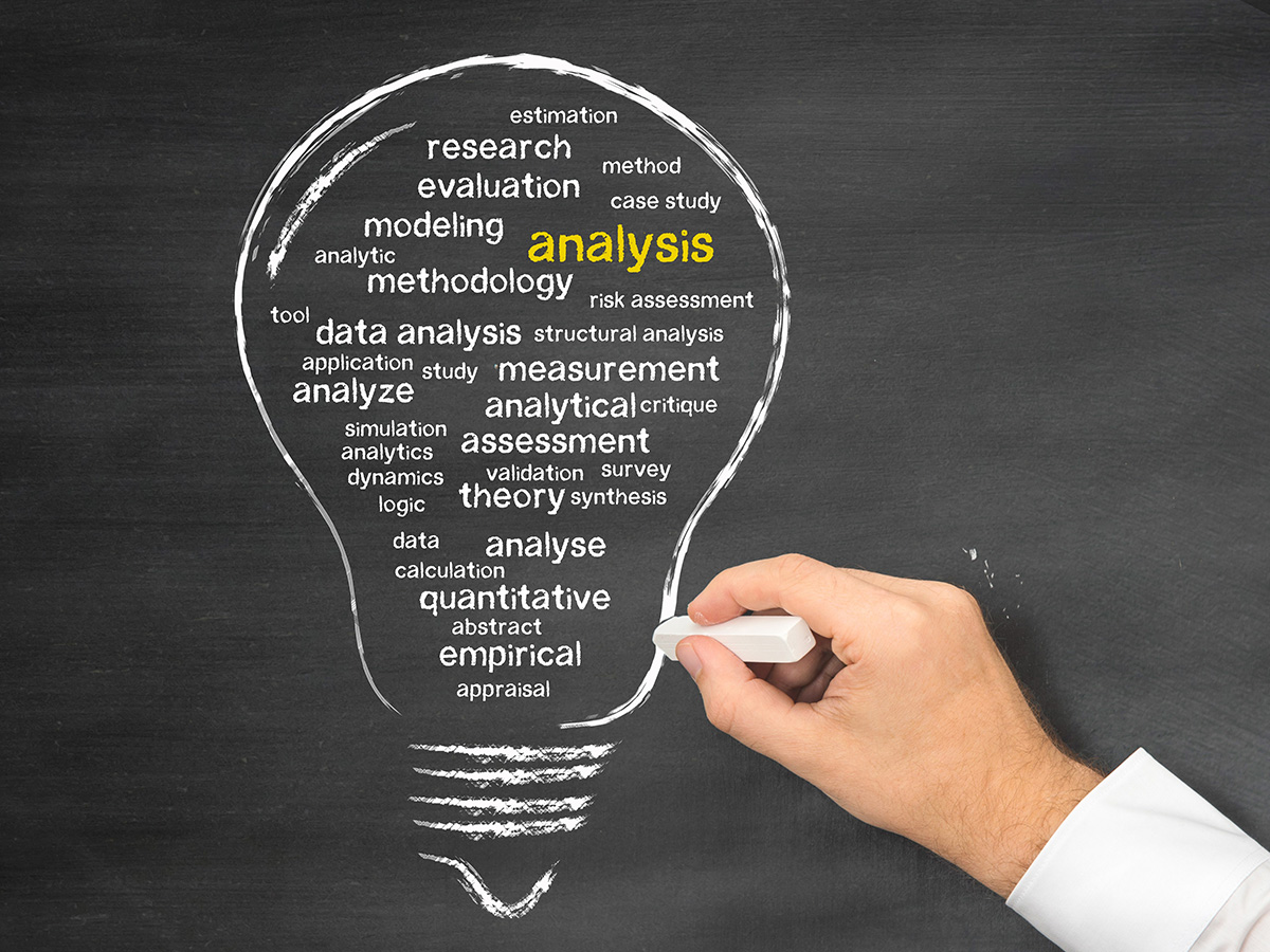 Hand holding chalk drawing a lightbulb outline filled with analysis-related keywords on a blackboard.