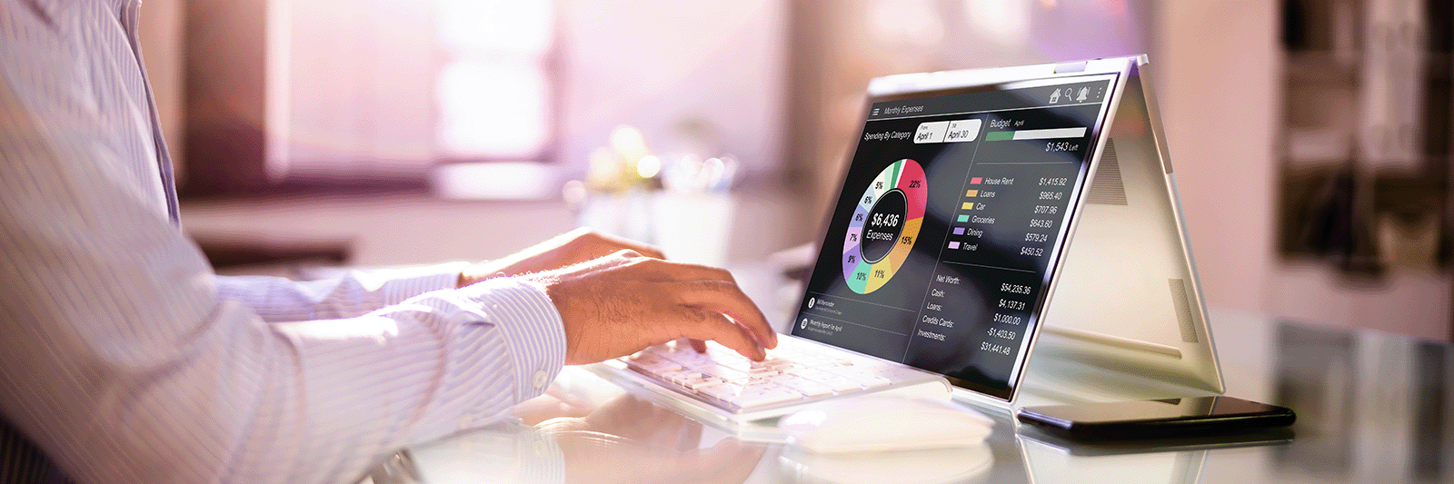 Person typing on a wireless keyboard connected to a tablet displaying a detailed monthly expenses pie chart and budget summary.