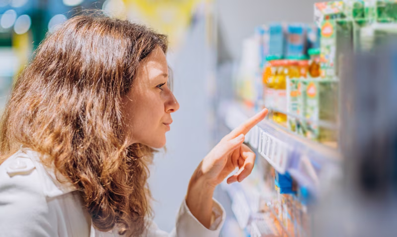 A woman looking intently at the products on a store shelf, pointing at an item.