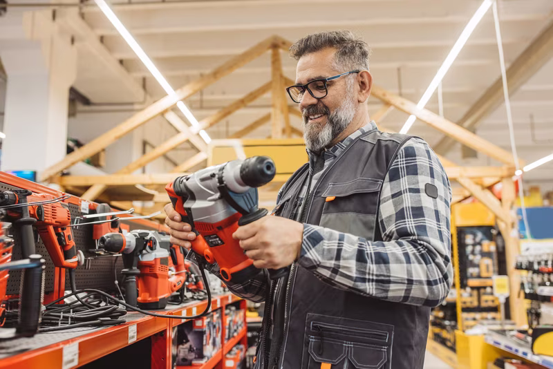 Smiling man holding a hammer drill in a hardware store.