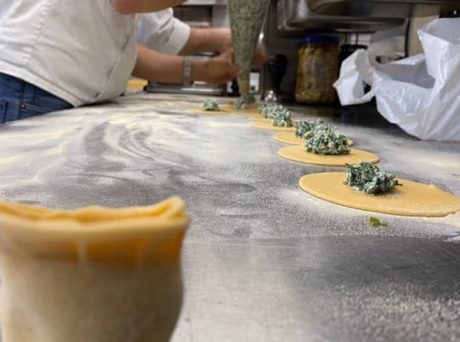 Jemand füllt Teigtaschen mit Spinat- und Käsefüllung auf einer bemehlten Arbeitsfläche in einer Küche.