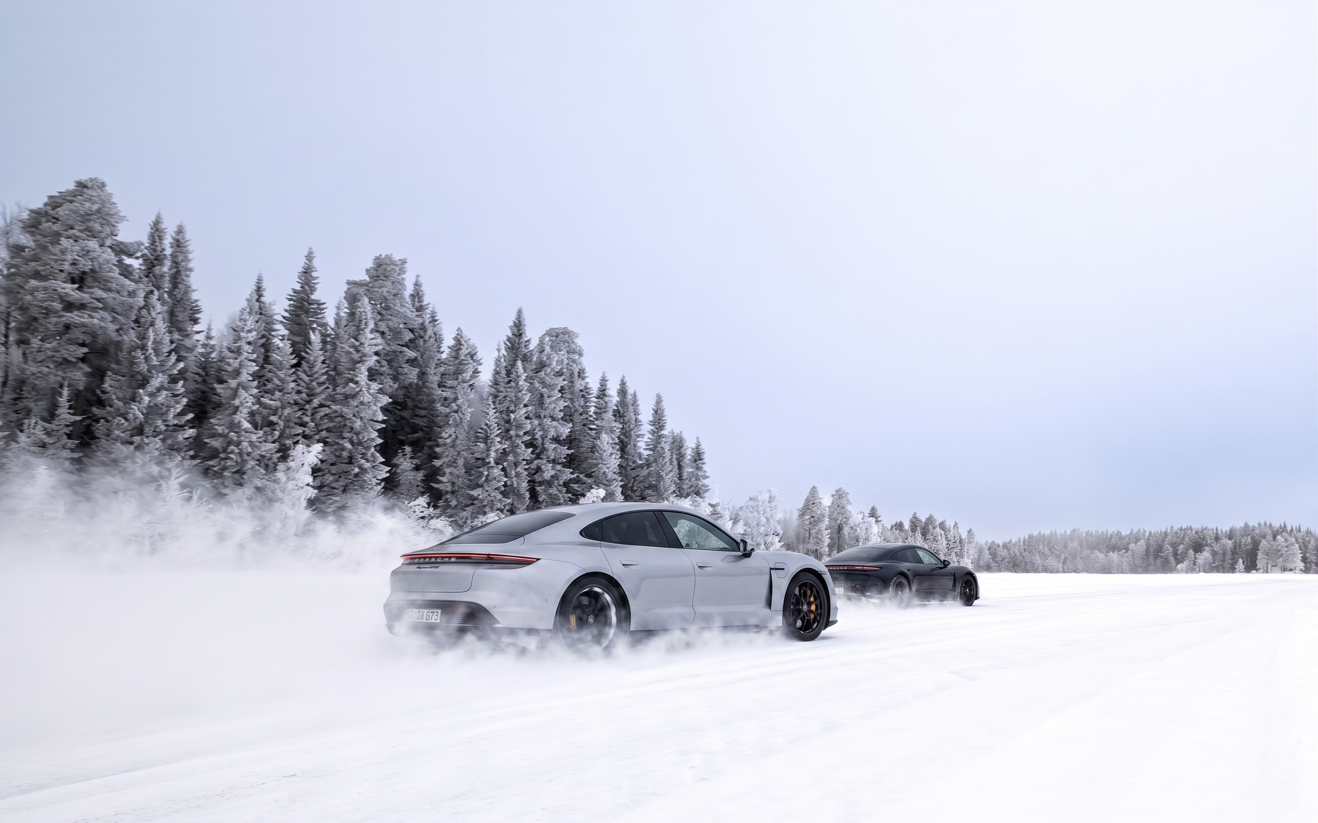 Black Audi station wagon drifting on a snowy road with snow spray and frosty trees in the background.