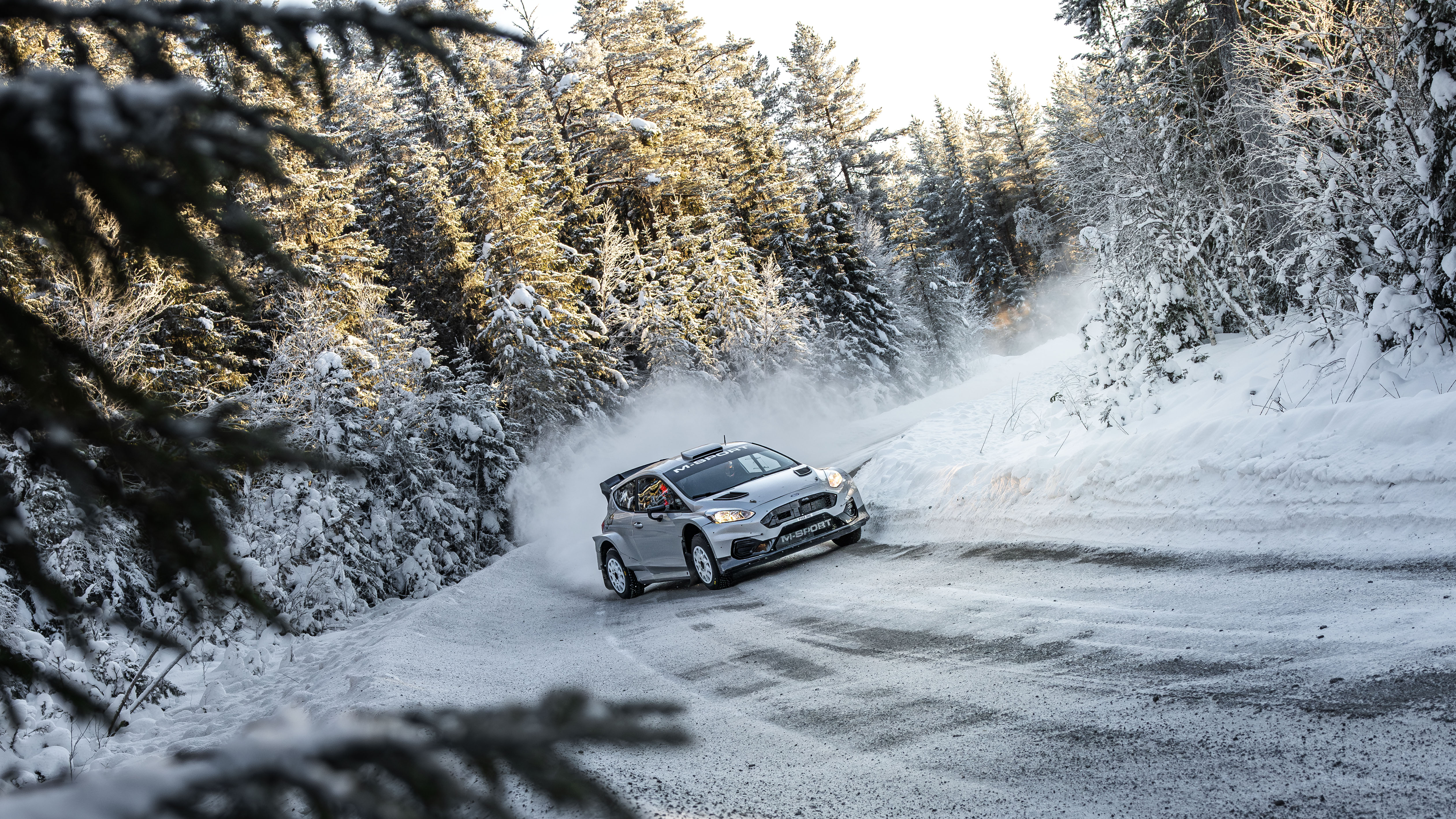 A rally test car kicking up snow while driving on ice in Jämtland, Sweden