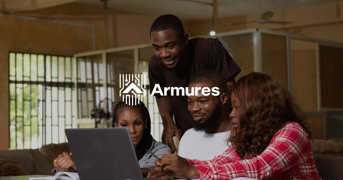Four young adults collaborating and looking at a laptop screen in a warmly lit room.