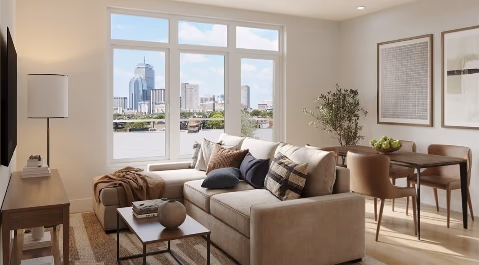 Modern living room with beige sofa, assorted cushions, wooden coffee table, dining table with chairs, and large window showing city skyline.