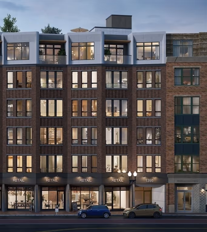 Modern multi-story brick apartment building with large windows and retail spaces on the ground floor at dusk, two cars parked in front.