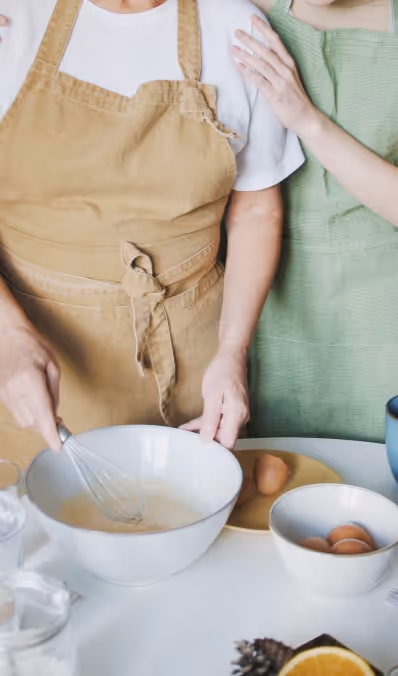 Two people in aprons preparing food, one mixing ingredients in a bowl with a whisk.