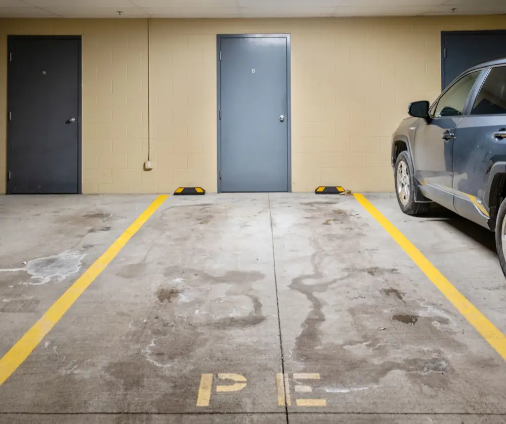 Empty concrete parking space labeled 'PE' between yellow parking lines, next to a black vehicle in an indoor garage.