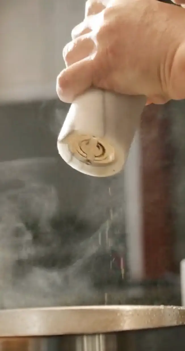 Hand sprinkling salt from a salt grinder over steaming food in a pan.
