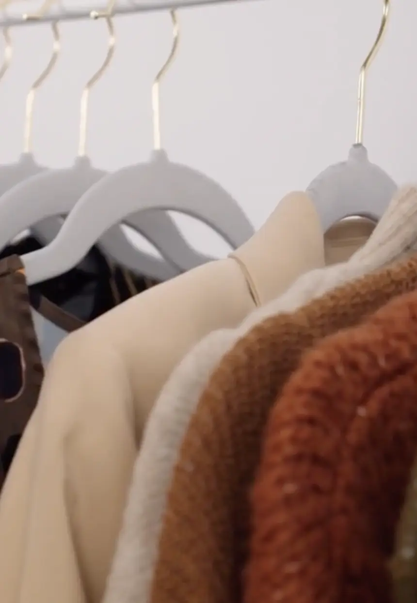 Close-up view of clothes on gray hangers, including neutral and brown knitwear and jackets.
