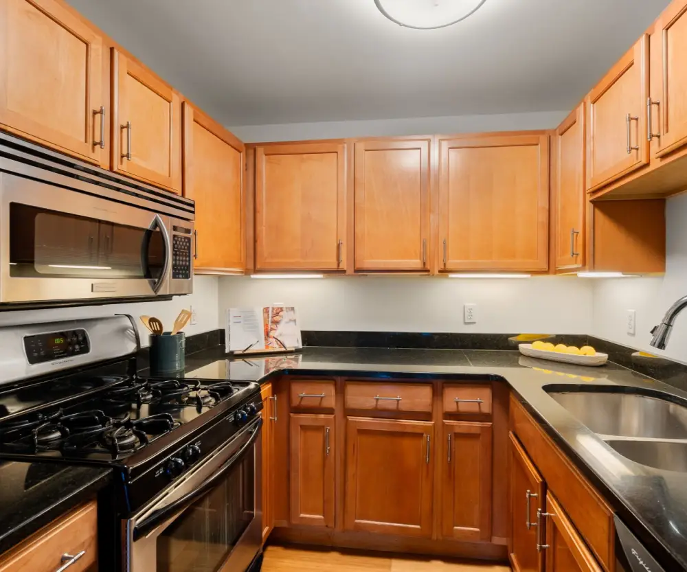 Modern kitchen with wooden cabinets, black granite countertops, stainless steel gas stove, microwave, and double sink.