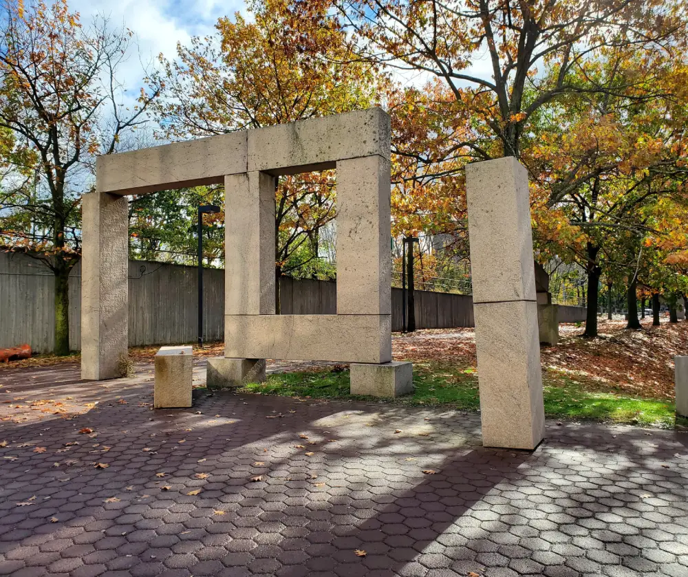 Large rectangular stone sculpture installation in a park with autumn trees and fallen leaves.