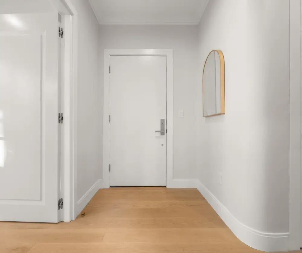 Minimalist entryway with white door, light wood floor, and arched mirror with wooden frame on the wall.