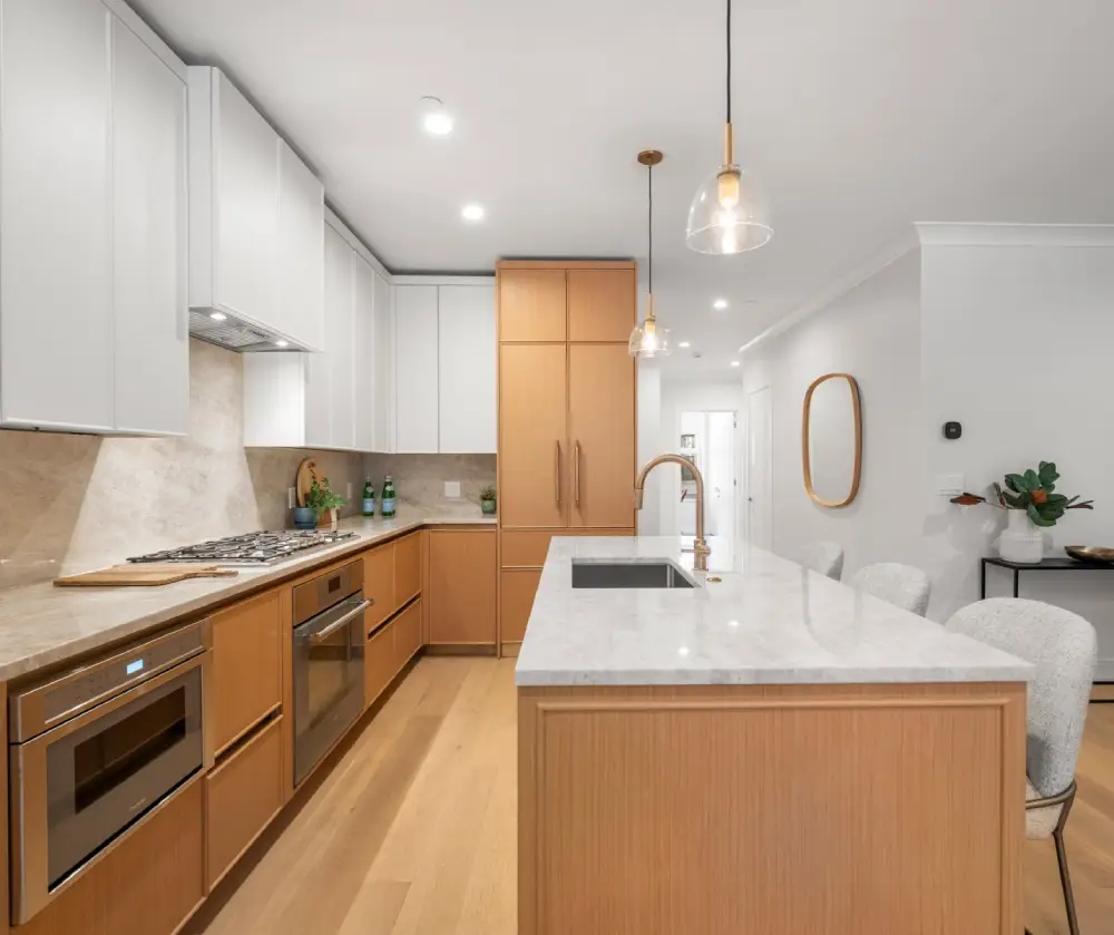 Modern kitchen with wooden lower cabinets, white upper cabinets, marble countertop island with sink, and pendant lights.