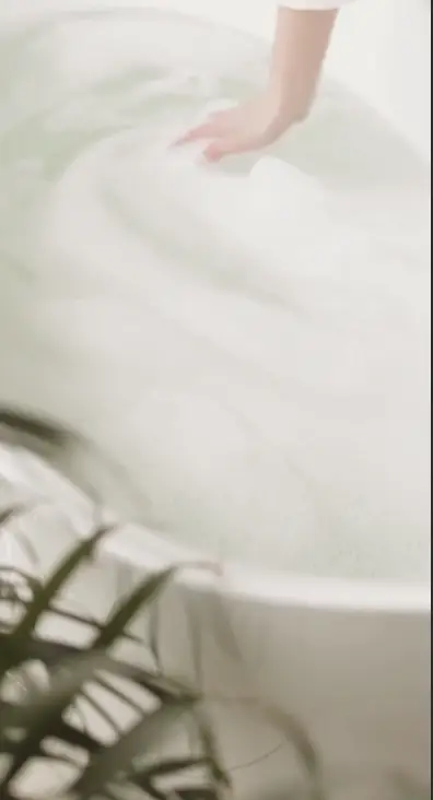 Hand smoothing a white towel resting on the rim of a bathtub filled with water.