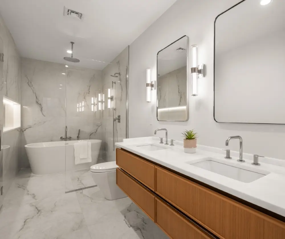 Modern bathroom with marble flooring, double sink vanity with wooden cabinets, two mirrors with lights, glass-enclosed shower, and freestanding bathtub.