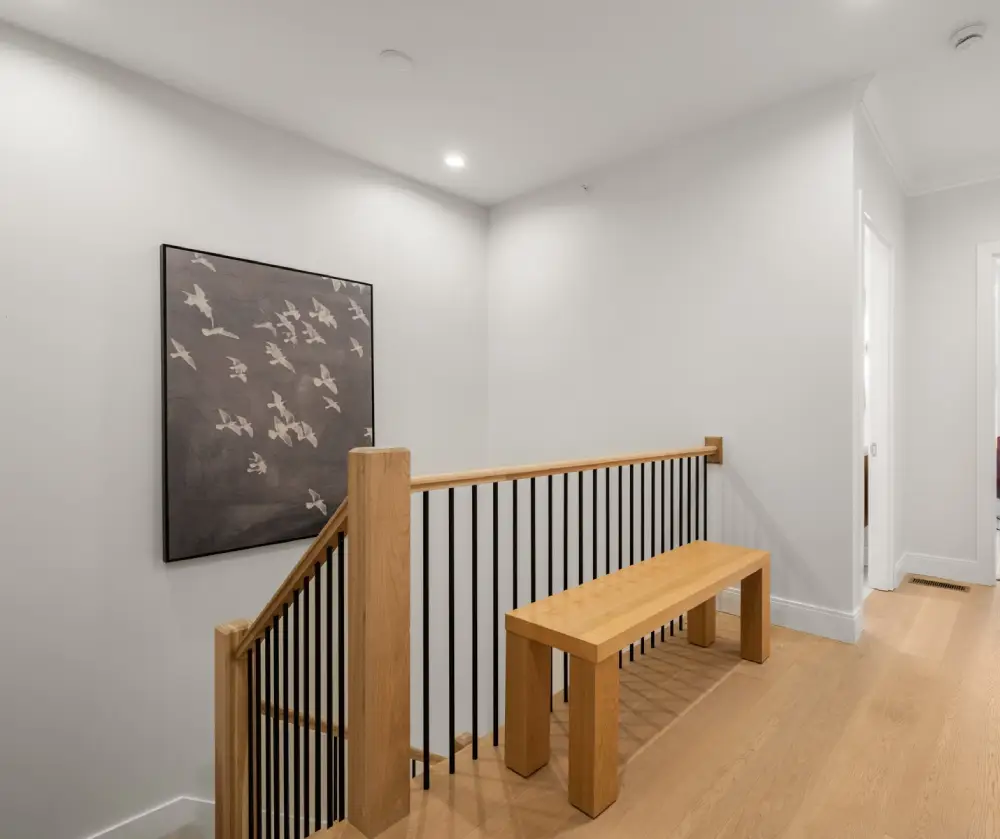 Minimalist hallway with a wooden bench, black metal balusters, and wall art depicting flying birds.