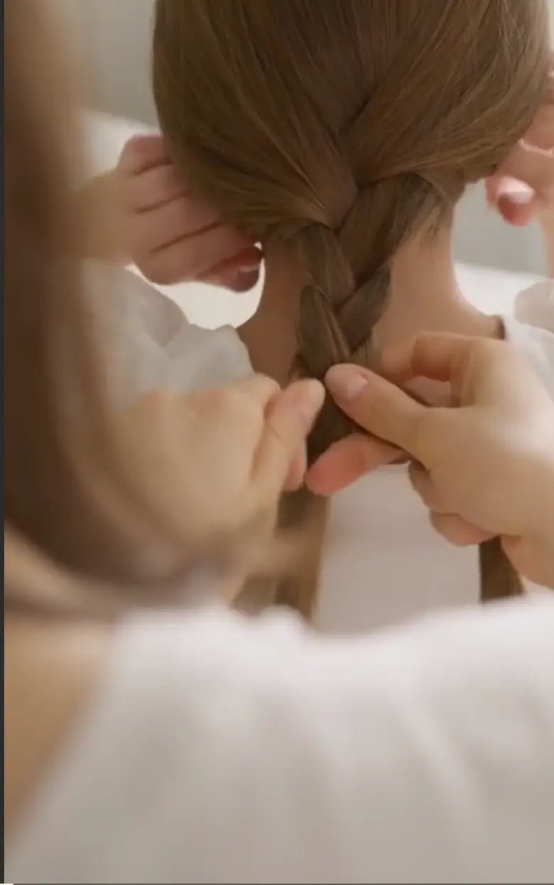 Person braiding another person's long brown hair from the back.