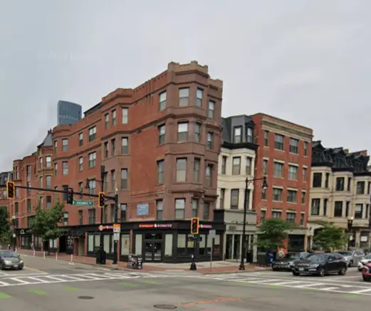 Street view of a corner building with Dunkin' Donuts and adjacent historic brick buildings in an urban setting.