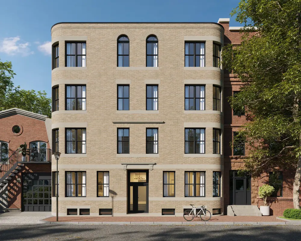 Modern four-story beige brick apartment building with curved corners, black-framed windows, a central entrance, a white bicycle parked outside, and surrounding trees.