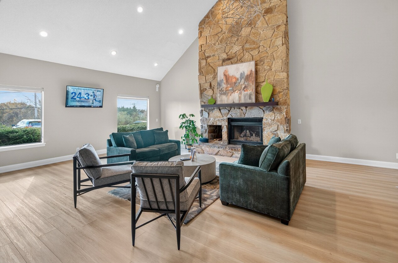 Bright living room with stone fireplace, green sofas, gray armchairs, round coffee table, and wooden floor.