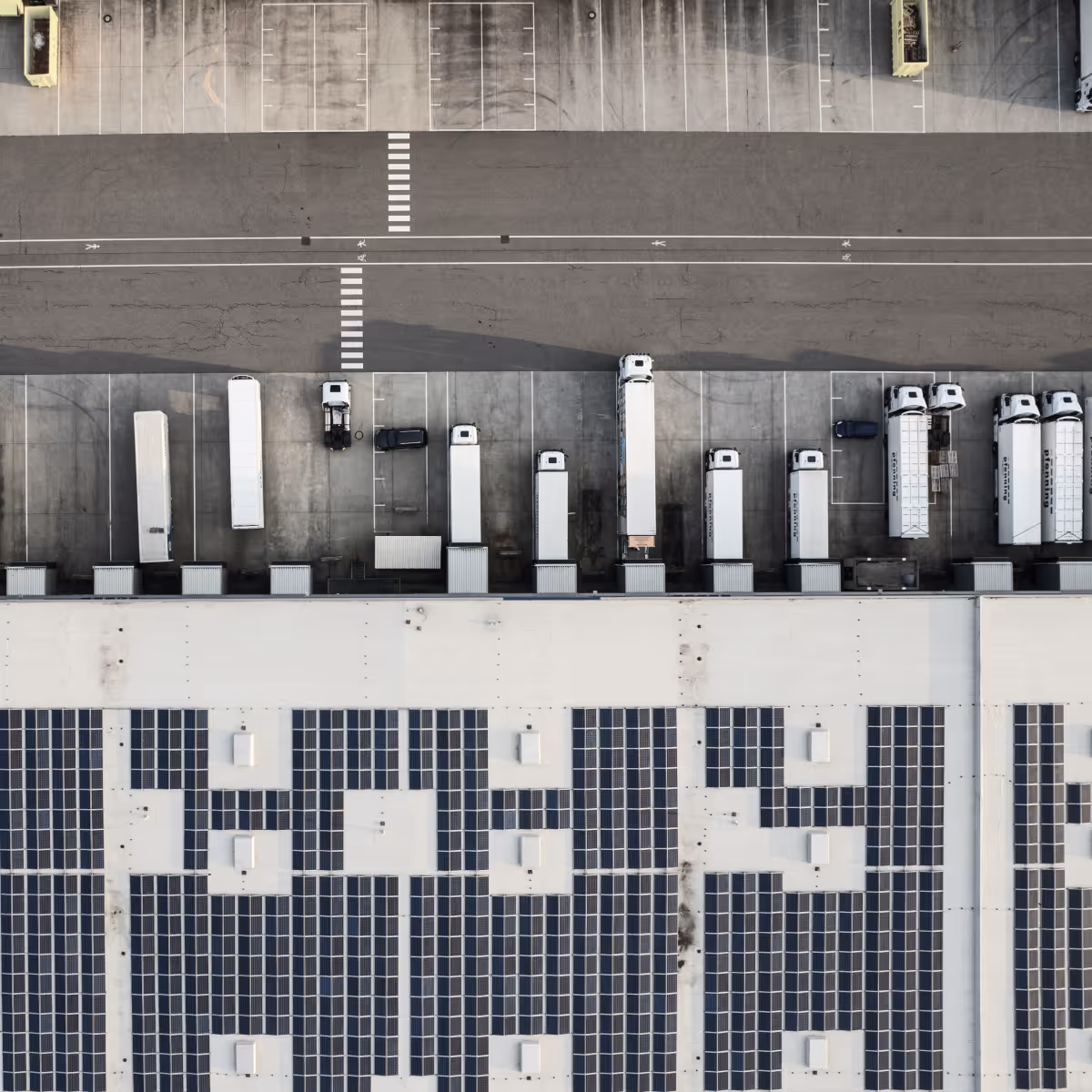 Vista aérea de un centro logístico industrial con camiones de carga y sistemas de energía, representando operaciones industriales modernas