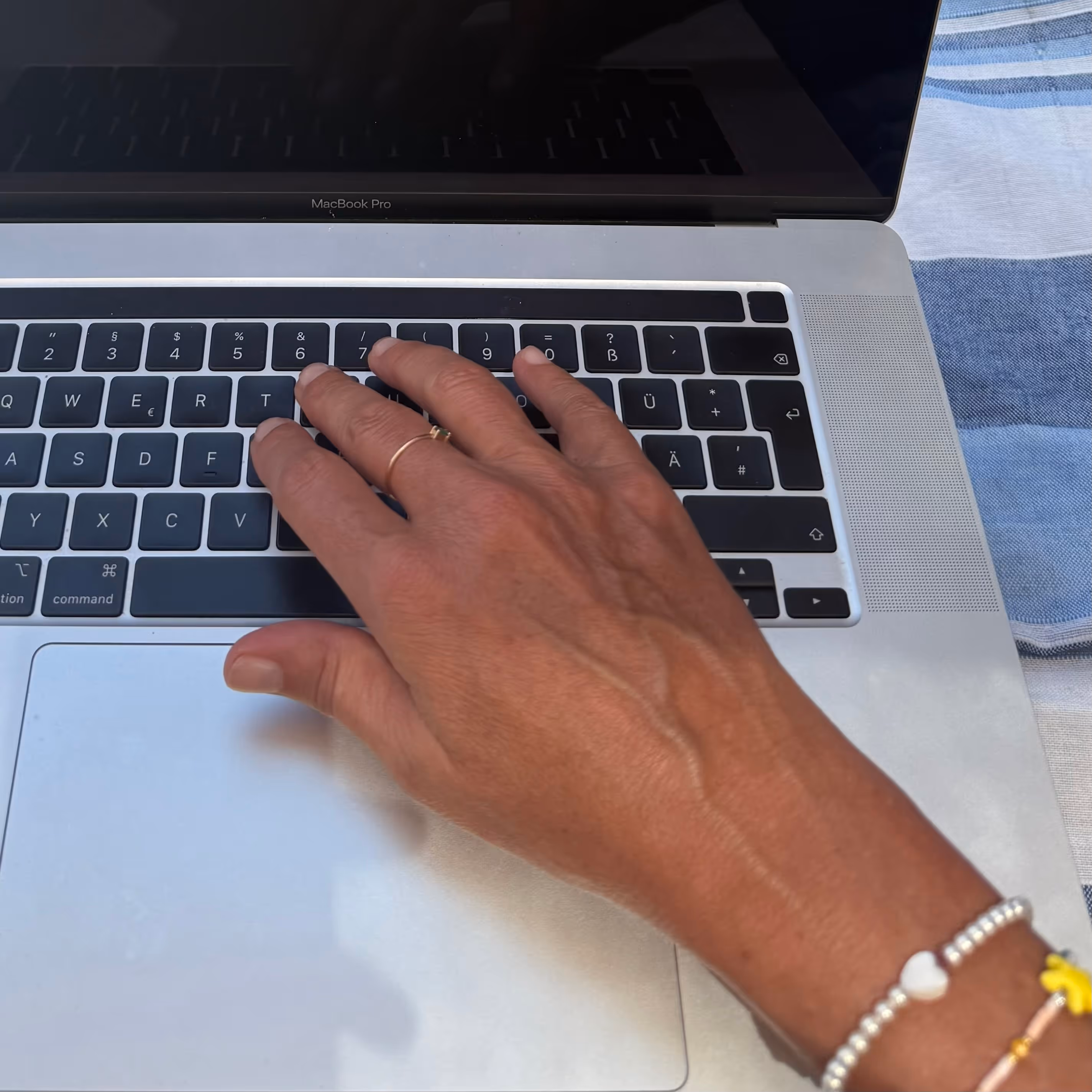 Hand mit goldenen Ringen und Armbändern auf der deutschen MacBook Pro-Tastatur.