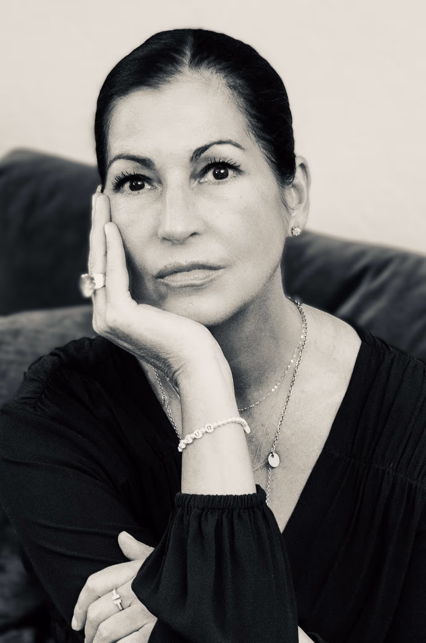 Schwarz-weiß-Porträt einer nachdenklichen Frau mit dunklen Haaren, die ihr Gesicht mit der Hand stützt.