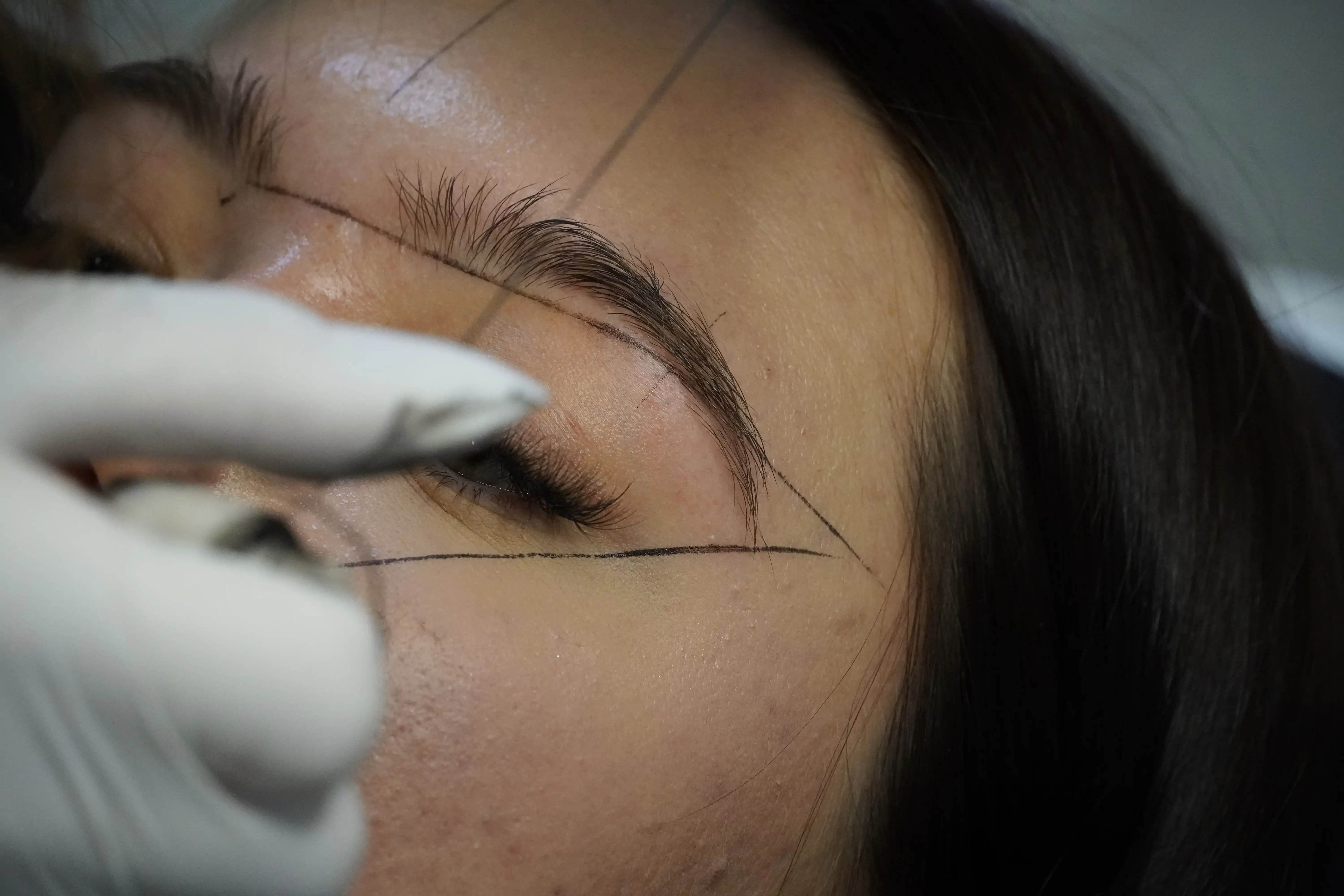 Nahaufnahme einer Person, deren Augenbraue mit einer Pinzette gezupft wird, während sie die Augen geschlossen hält.