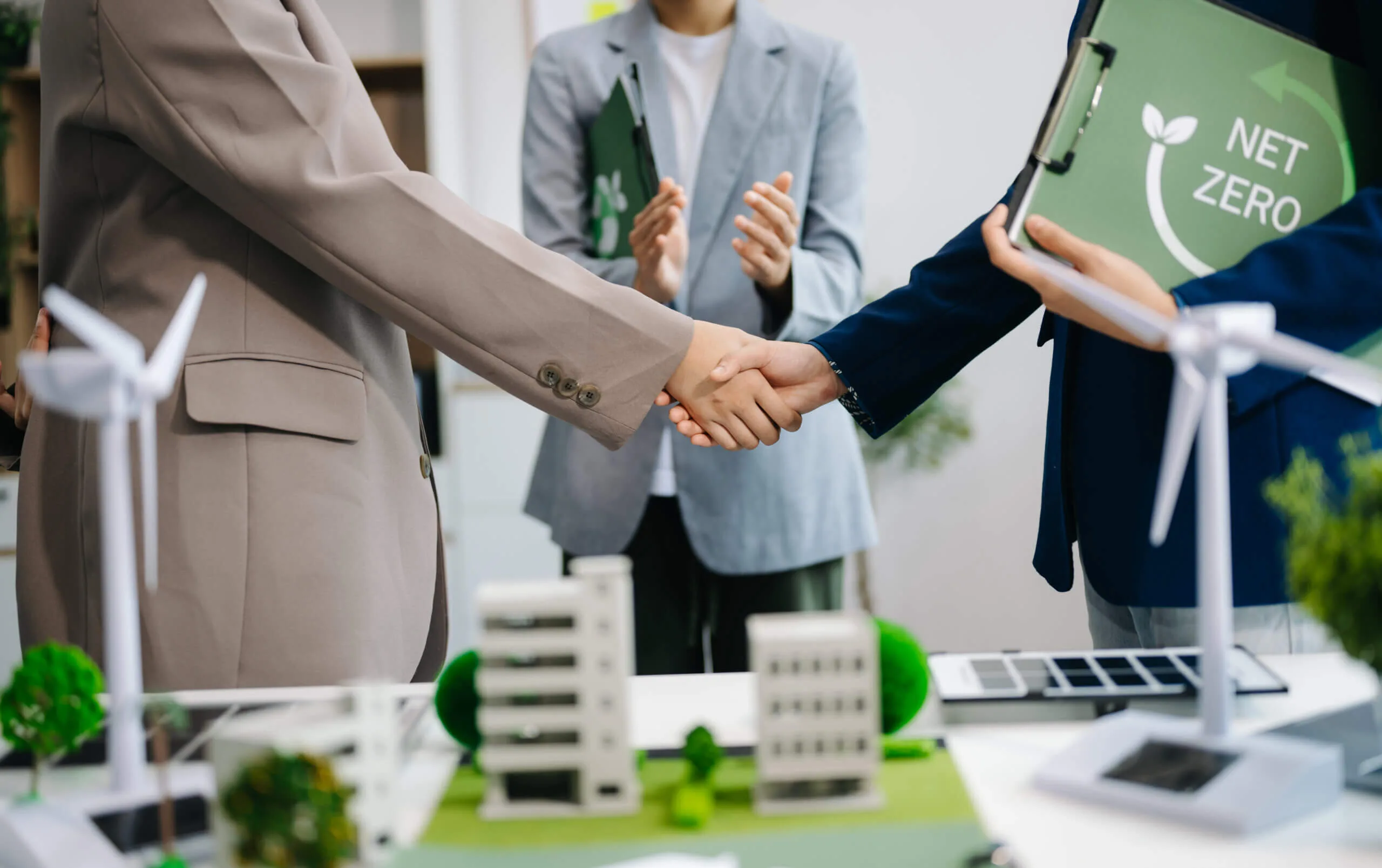 People shaking hands in front of green houseing model