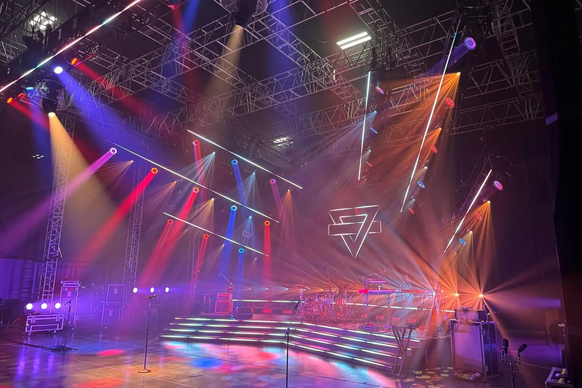 Empty concert stage with colorful spotlights and illuminated steps under a metal truss ceiling.