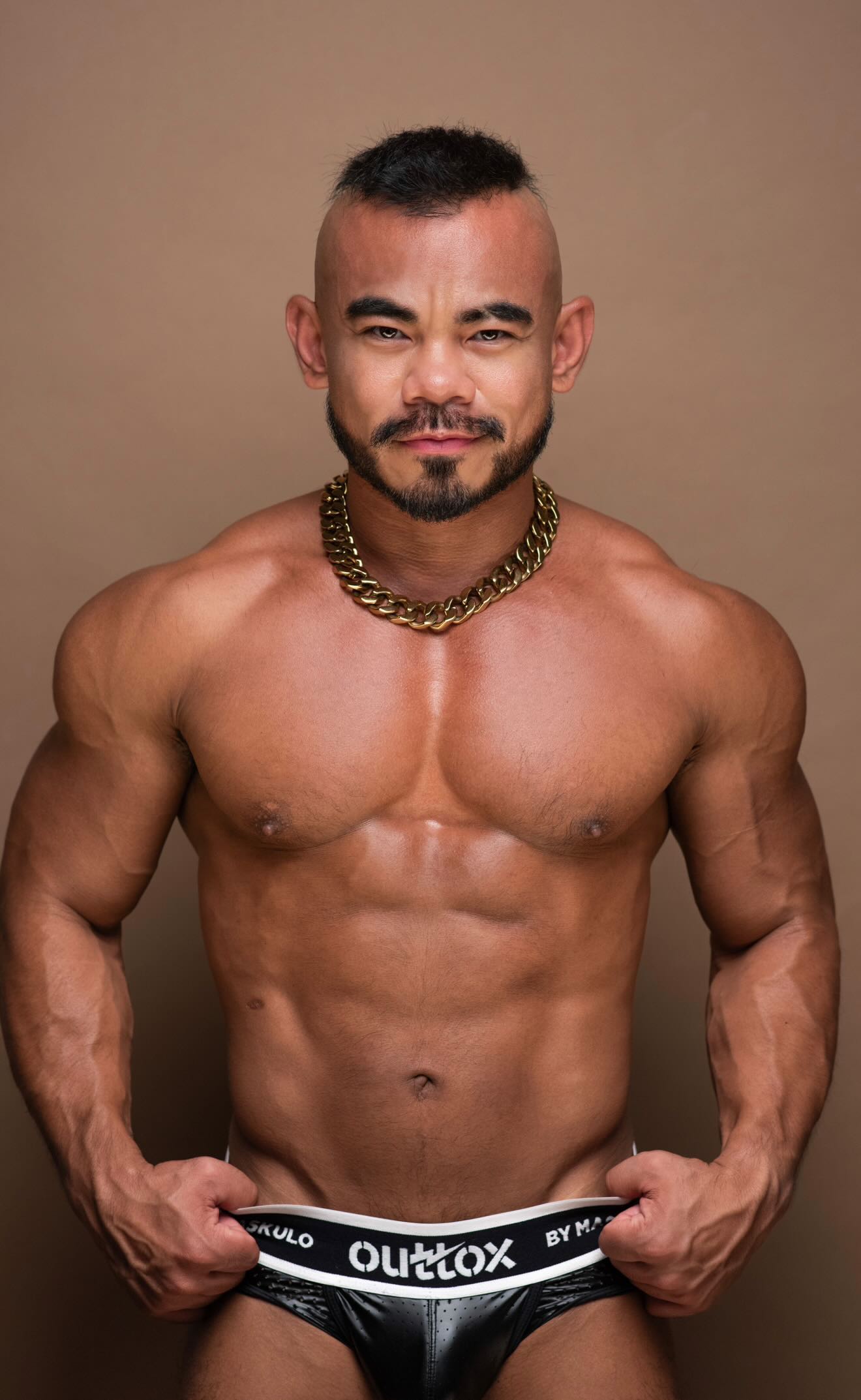 Jason smirks in a gold chain necklace with intimidating muscles