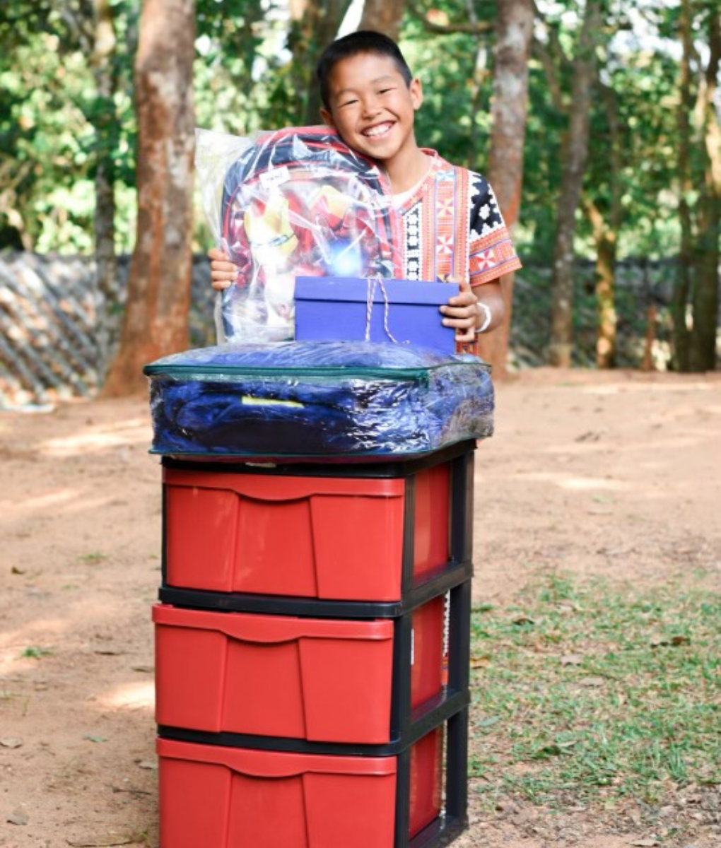 Child holding donated supplies and gift items stacked in containers.