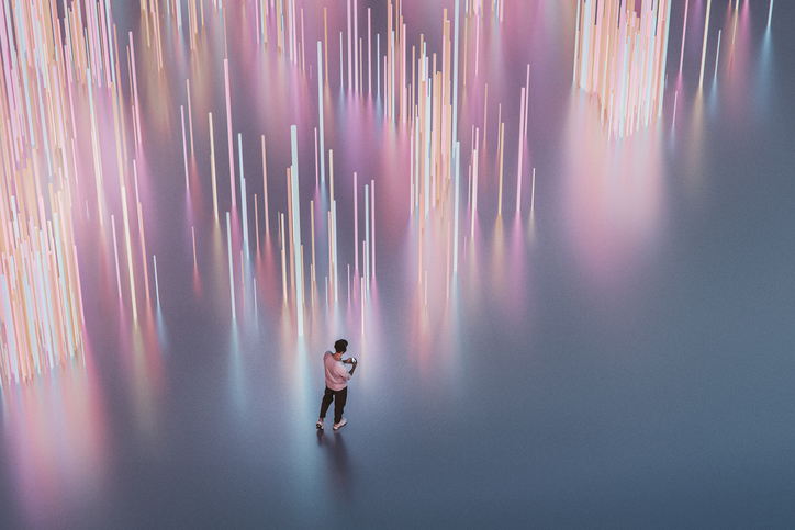 Person standing on a reflective surface looking at a phone surrounded by vertical glowing light bars in pink and orange hues.