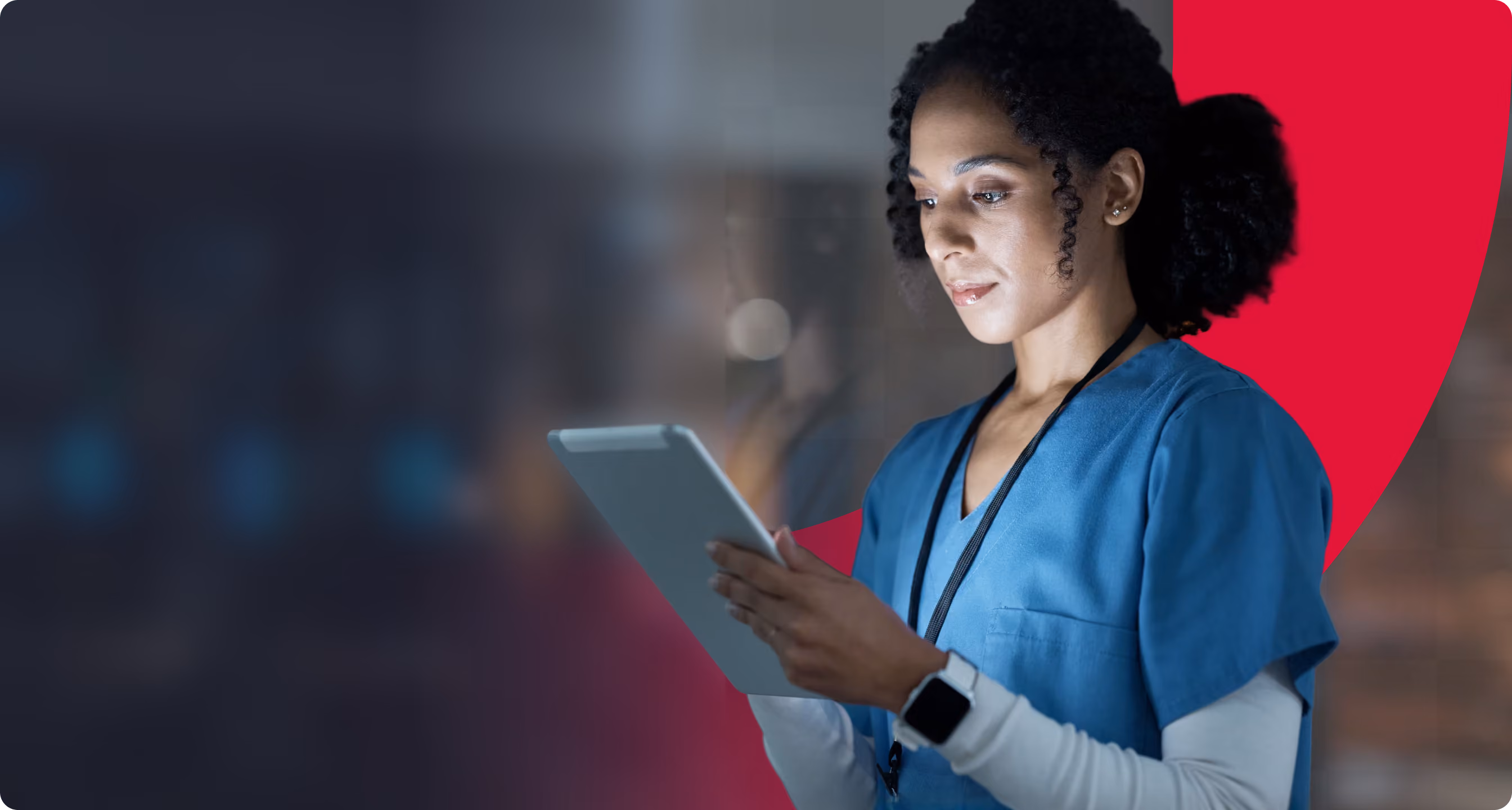 Female healthcare professional in blue scrubs looking at a tablet device, with a dark blurred background and a red curved shape behind her.