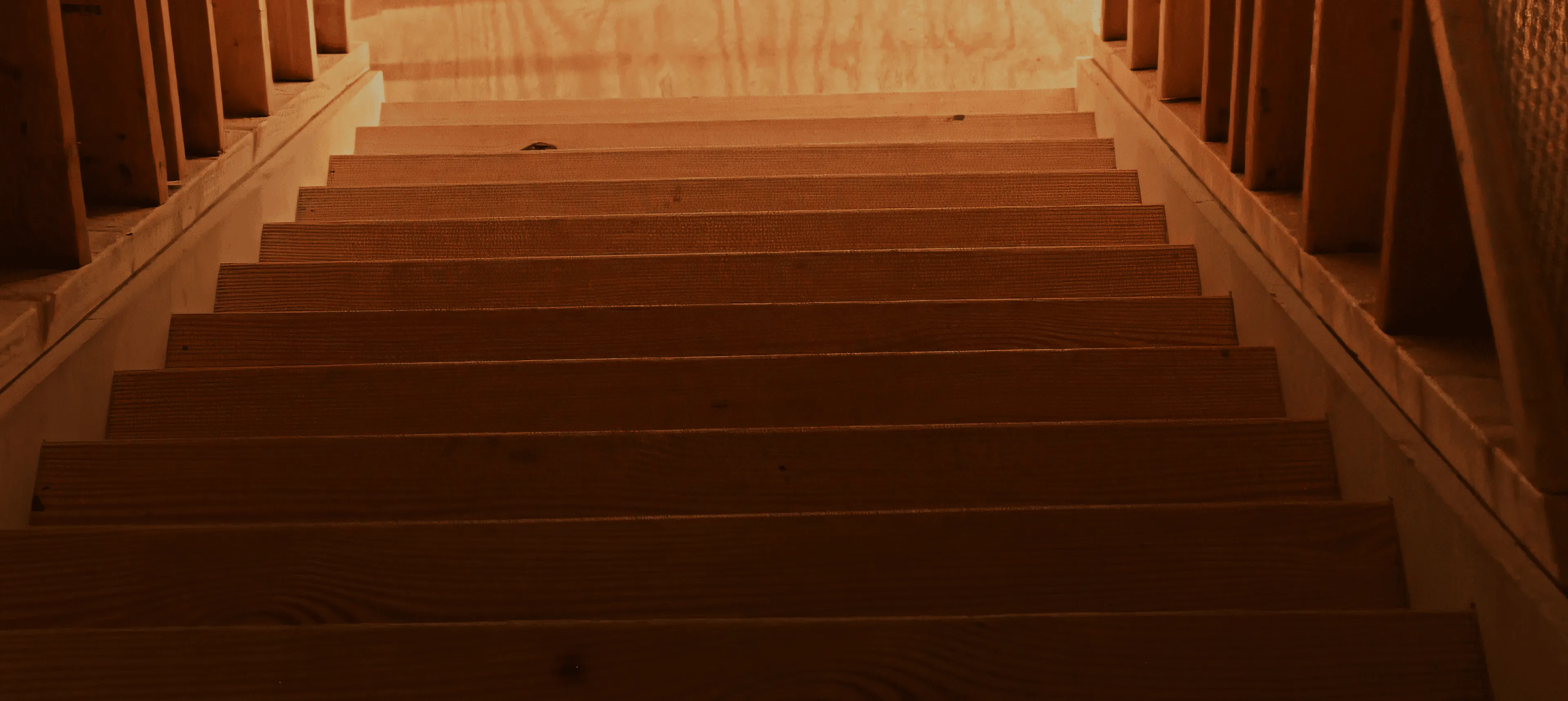 View looking down a wooden staircase with railings on both sides and warm lighting.