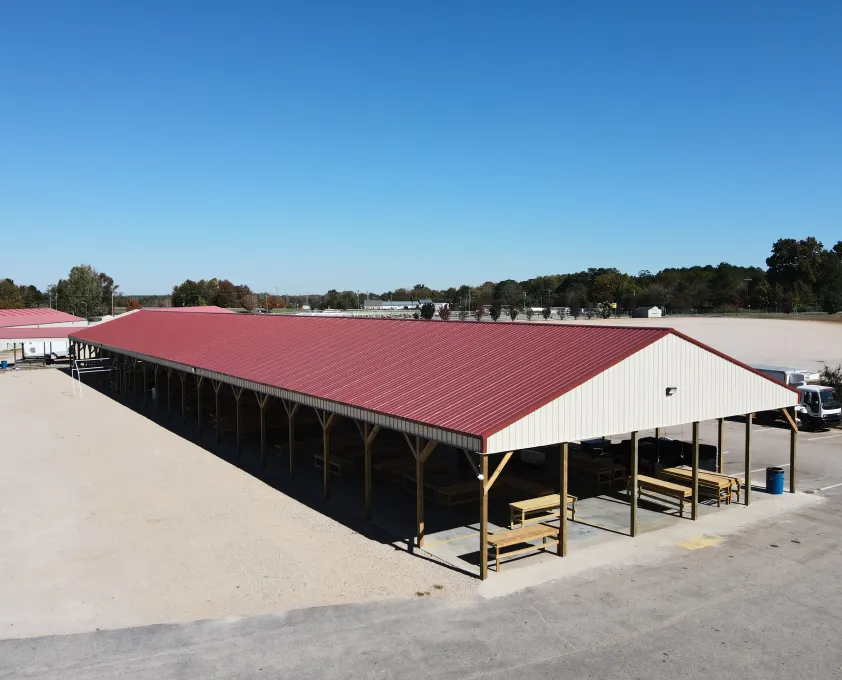 Large commercial open-air pavilion with a red roof and wooden support beams, located on a gravel and paved area.
