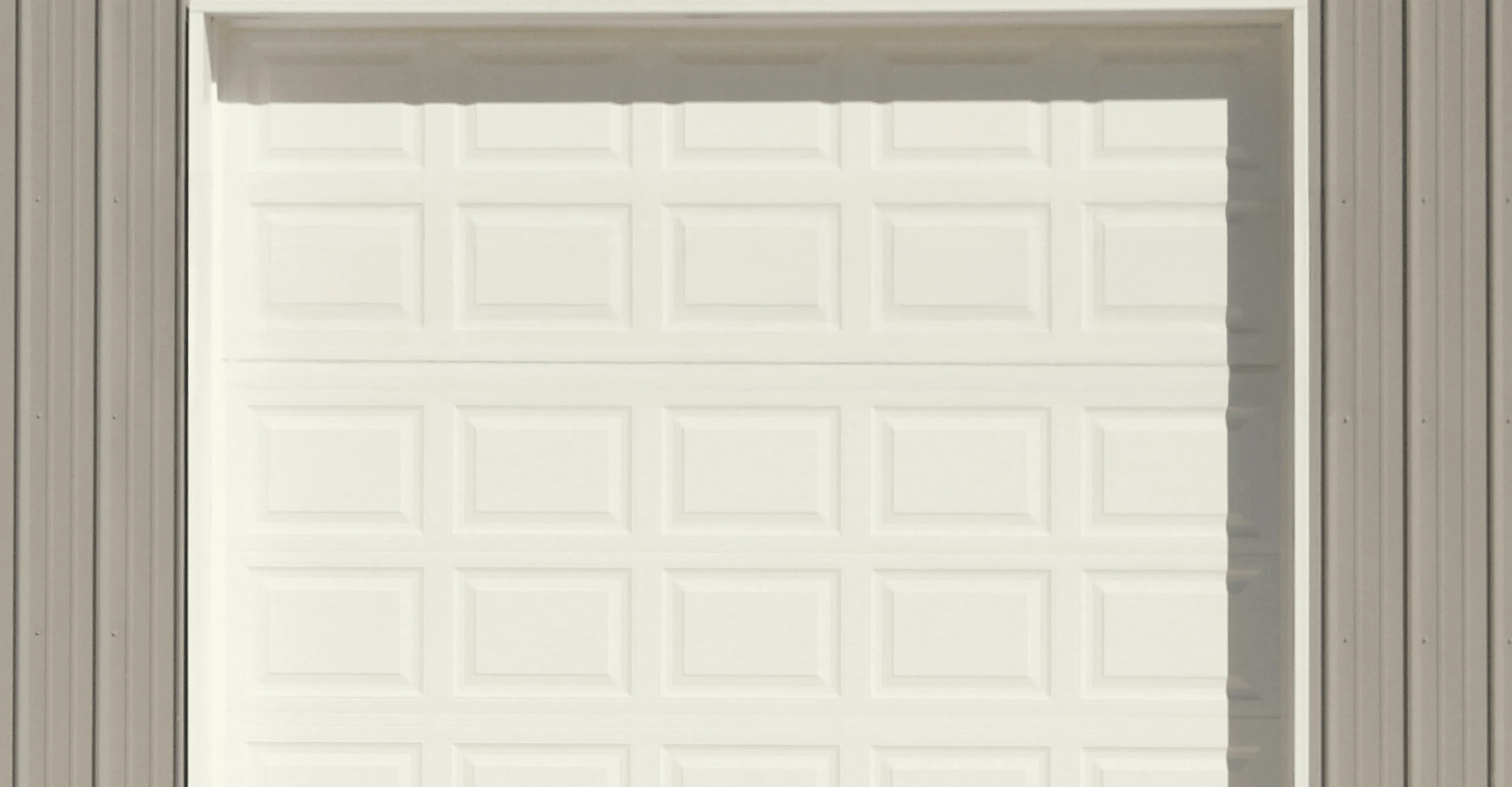 White garage door with four small windows along the top and gray siding on both sides.