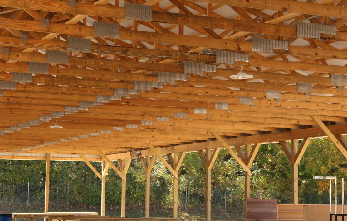 Wooden pavilion roof structure with multiple exposed beams and support columns outdoors.