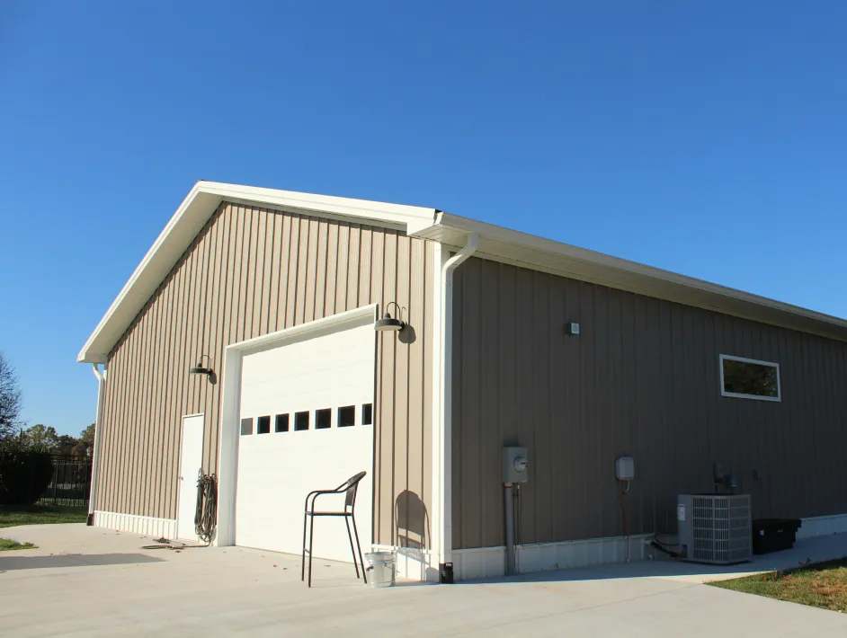 Large beige metal building with a white garage door, and an air conditioning unit on a concrete driveway.