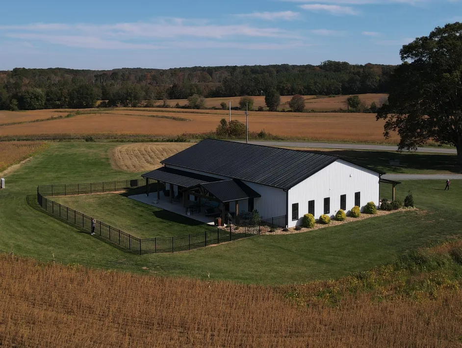 White building with a black roof surrounded by a fenced green lawn and fields.